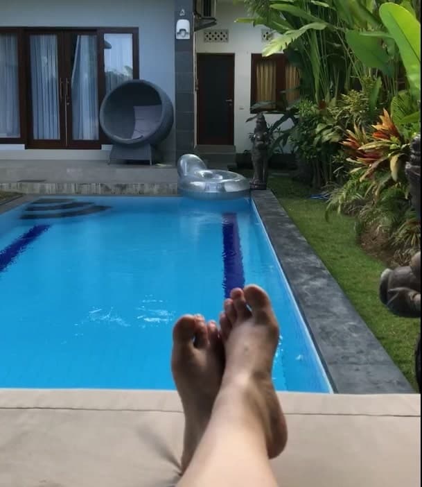 Person resting by a backyard pool with feet up.