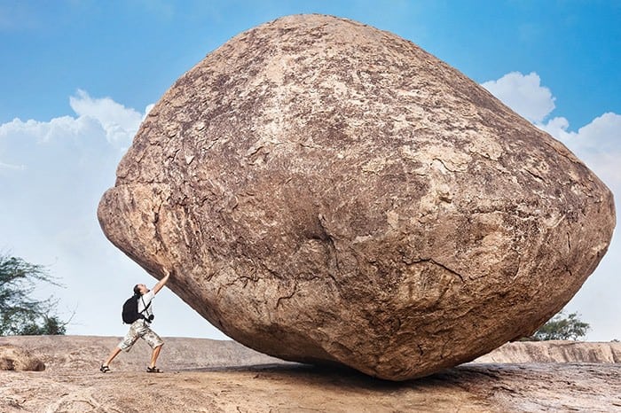 Person pushing a huge boulder on rocky ground